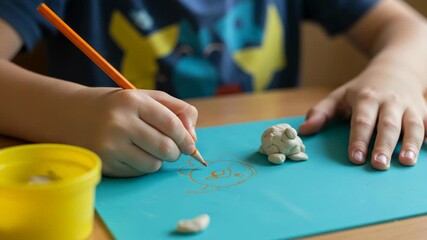 Childs hands sculpting clay with a pencil on a blue paper - Powered by Adobe