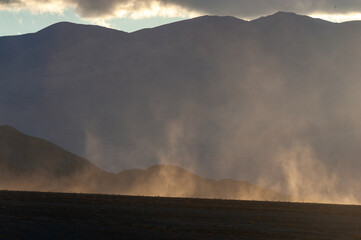 Back-lit sand blowing up by heavy winds near stovepipe wells in Death Valley national park, California.