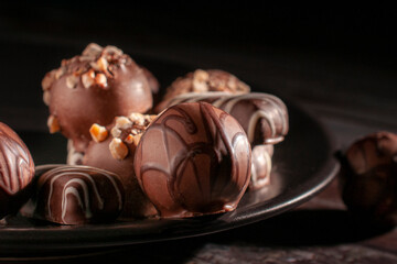 Assortment of chocolates on a dark plate and black background, chiaroscuro or Renaissance technique, Baroque style. Dark food macro photogrfaphy