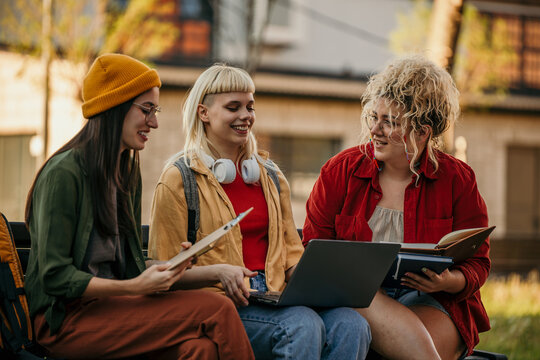 University students collaborating on project outdoors using laptop and notes