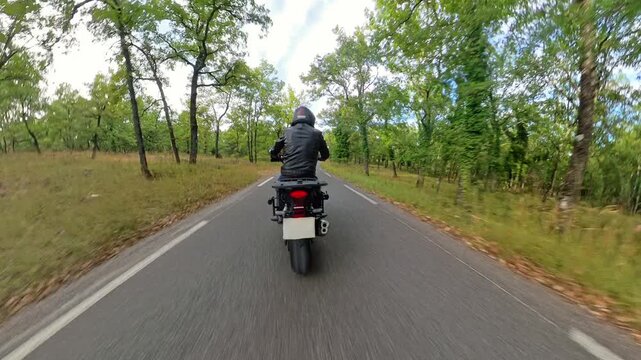 Biker riding on a winding road through a forest along cliffs