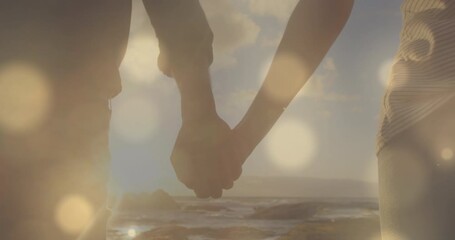 Animation of glowing spots over diverse couple holding hands - Powered by Adobe