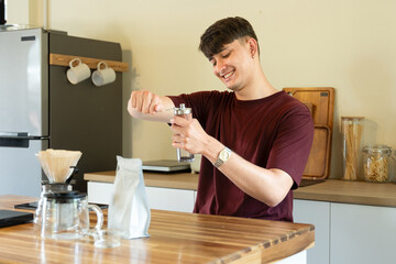 A man is grinding coffee beans in a coffee grinder. The coffee grinder is on a wooden table.