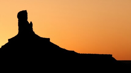 A striking silhouette of a prominent rock formation stands against a vibrant orange gradient sky,