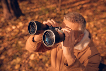 Amateur birdwatcher observing birds and other animals in nature with binoculars.
