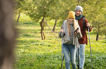 Happy young couple enjoying a hike in nature, using trekking poles and wearing winter clothes with...