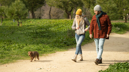 Young couple walking with their small dachshund dog in a park, enjoying a leisurely stroll on a...