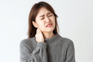 Young woman in a gray sweater grimaces in pain while holding her neck, indicating discomfort or stiffness against a plain white background