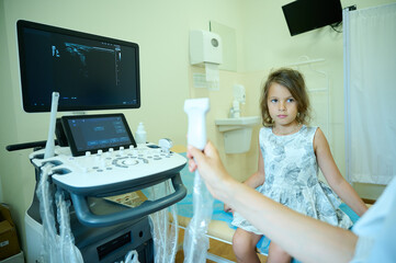Caring pediatrician holding ultrasound probe consulting little child in medical clinic. Doctor...