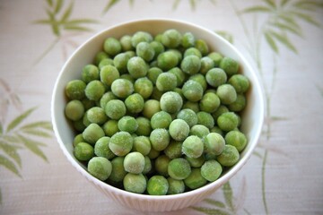Close-up of frozen green peas in a white bowl placed on a table with copy space, healthy vegetable concept.