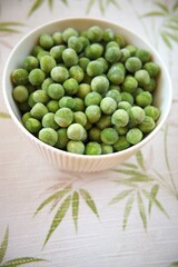 Close-up of frozen green peas in a white bowl placed on a table with copy space, healthy vegetable concept.