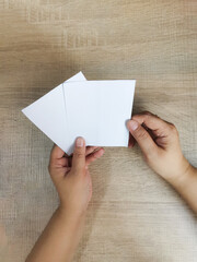 Hands holding two sheets of white paper on a wooden surface, implying creativity. Copy space.