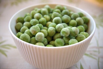 Close-up of frozen green peas in a white bowl placed on a table with copy space, healthy vegetable concept.