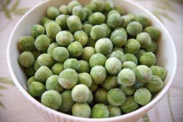 Close-up of frozen green peas in a white bowl placed on a table with copy space, healthy vegetable concept.