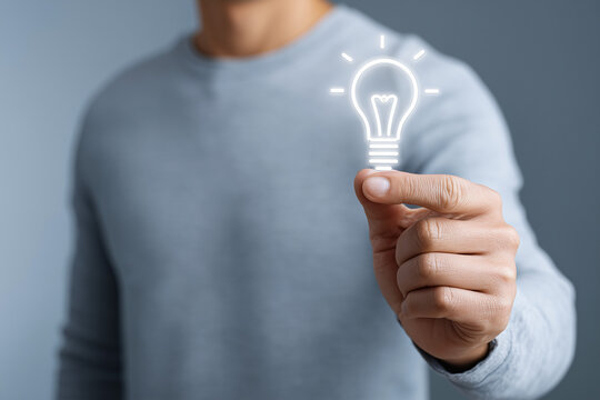 A person holding a glowing light bulb, representing idea or innovation. The person is wearing a gray sweater, symbolizing the human element behind this concept. 