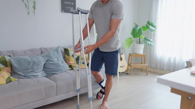 Injured Asian handsome man wearing leg splint, walking with crutches
