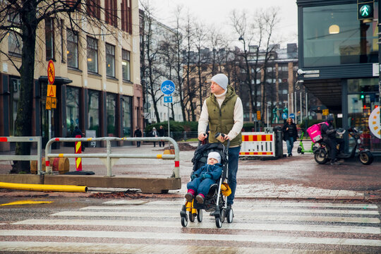 Chilly autumn city: dad pushes toddler stroller across wet streets, raw urban winter vibes, cold rainy day family moment.