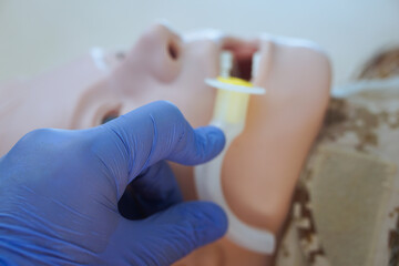 Blue-gloved hand measuring an oropharyngeal airway tube against a medical training mannequin in a...