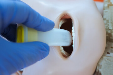 A gloved hand inserting an oropharyngeal airway tube into a medical training mannequin in...
