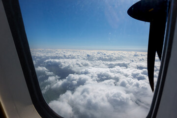 Plane propeller and white puffy cloud under blue sky through plane window