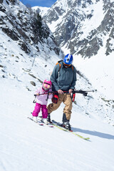 Smiling little girl skiing with her father with mountains on the background.