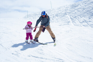 Father teaching his little daughter how to snowplow ski on a beautiful sunny day.
