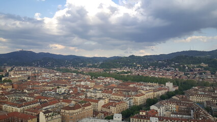 Naklejka premium A panoramic view of the Torino skyline, with rays of sunlight breaking through the clouds and the majestic Alps visible in the background.