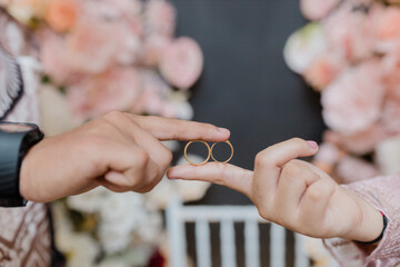 A close-up photo of two hands holding a pair of gold wedding rings together. One hand belongs to a man and the other to a woman, symbolizing love, unity, and commitment.