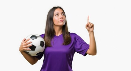 A young woman in a purple soccer jersey holding a ball, pointing upwards with her index finger.