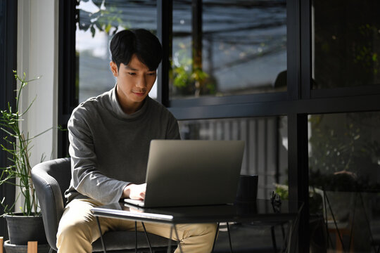 Focused freelance working in a relaxed indoor-outdoor area, dressed in smart casual, and using a minimalist setup