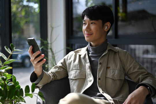 Portrait of a relaxed man listening to music or a podcast, seated by the window with natural light and greenery