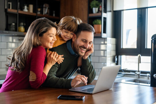 Happy young family with kids in kitchen have fun using modern laptop together, enjoying weekend