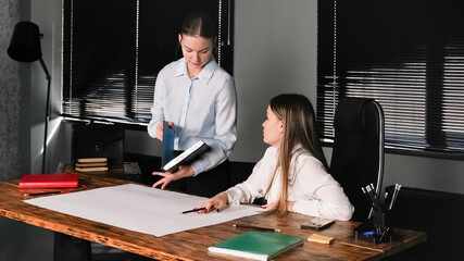 Two women collaborate on a project in a modern office setting during daylight hours