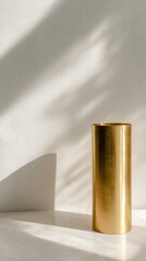 Golden cylinder vase on a light surface with sun shadows