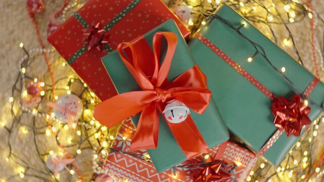 Close-up of Christmas presents with red and green wrapping, ribbons, lights and festive ornaments on the floor.
