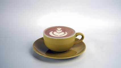 Artisan pink latte with rosetta foam art in a yellow ceramic cup