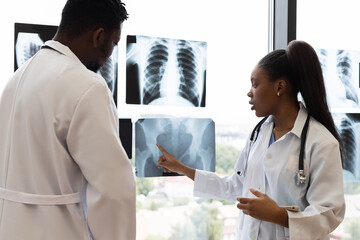 Male and female doctors analyzing x-rays together in a well-lit clinic environment near window. They are collaborating on reviewing medical images to determine diagnosis or treatment.