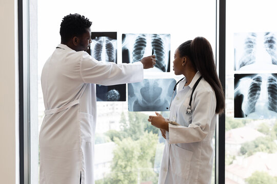 Medical professionals, male and female, reviewing x-ray diagnoses near a bright clinic window. Collaborative discussion over radiological findings indicates teamwork for accurate analysis. - Powered by Adobe