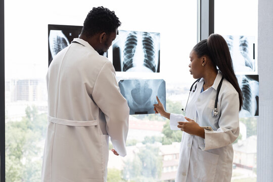 Male and female doctors of diverse backgrounds examining chest X-ray images by window. Collaborative medical consultation in modern clinic setting, emphasizing teamwork, analysis - Powered by Adobe