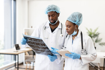 Healthcare professionals wearing medical scrubs and gloves evaluating diagnostic images in bright...