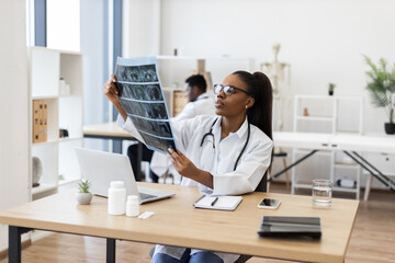 Confident young adult female doctor evaluating X-ray scans in office workspace. Medical...