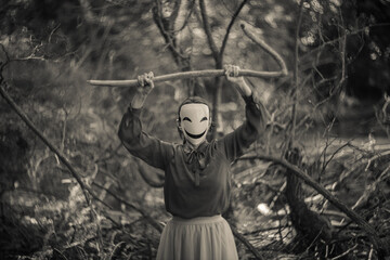 Mysterious figure wearing animegao mask holding branch in dark forest.