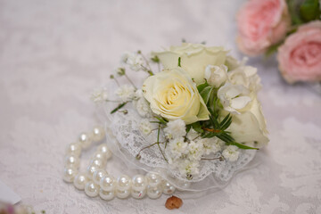 The image shows a white rose and gypsophila wrist corsage with a pearl bracelet.
A corsage is a small bouquet of flowers worn by a woman on her wrist or pinned to her dress for formal occasions like w
