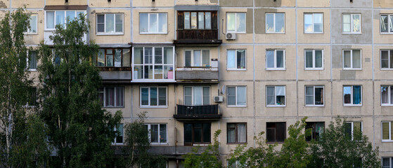 Facade of old Soviet-era apartment building with multiple windows and balconies, partially covered...
