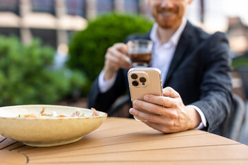 Red-bearded businessman drinking coffee while browsing phone