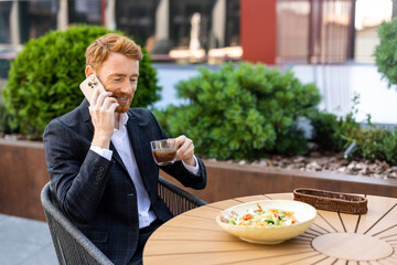 Red-haired businessman talking on phone while drinking coffee