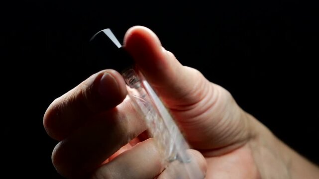 A small glass test tube with liquid inside.
Making perfume in a convenient and compact bottle.
A mini perfume tester close-up in a man's hands
