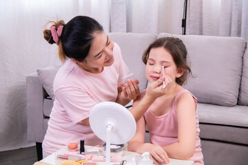 Asian single mother applying eyeshadow to daughter with smile, bonding moment during makeup routine, family care atmosphere highlighting gentle treatment, affection and confidence in daily lifestyle