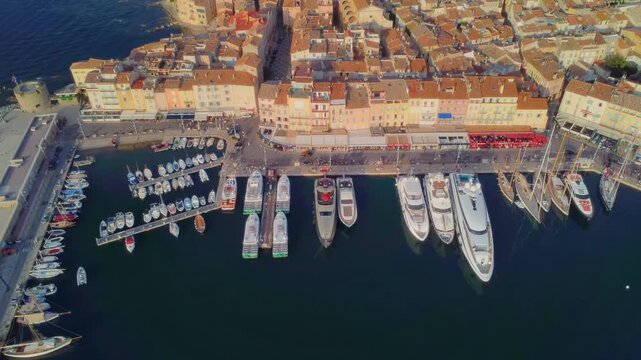 aerial drone shot capturing the iconic Port of Saint Tropez on the French Riviera, showcasing a vibrant array of luxury yachts and traditional fishing boats moored alongside the charming, historic tow