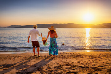 A happy family on holidays stands on a beautiful beach in the mediterranean sea and enjoys the summer sunset time
